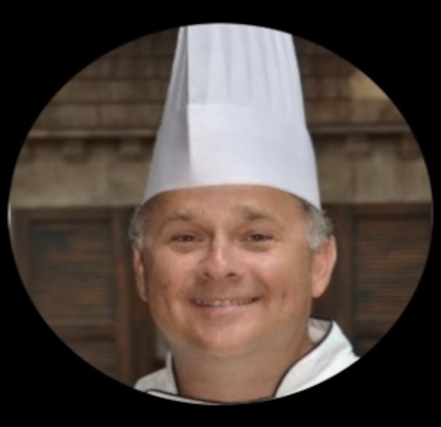 A man wearing a chef's hat is smiling.